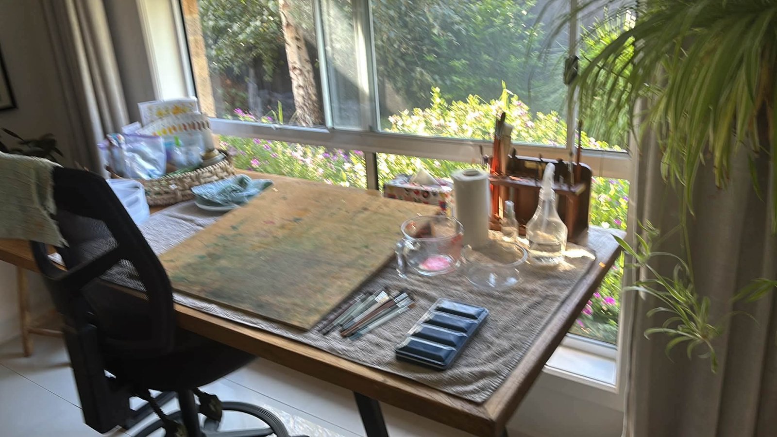 Robyn Holland's watercolour studio: a paint-worked table set with brushes and paints beside a sunlit garden window